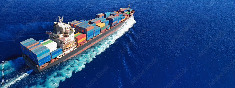 Aerial drone ultra wide panoramic view above huge colourful container carrier vessel cruising deep blue open ocean sea
