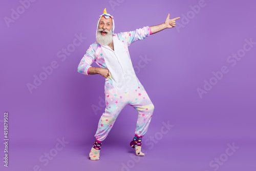 Full length body size view of attractive cheerful man in pajama pointing copy space dancing isolated over violet purple color background