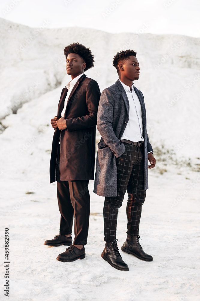 Two trendy african american men, in suits, men posing together outdoors against the background of chalk mountains Two trendy african american men, in suits, men posing together outdoors against the background of chalk mountains