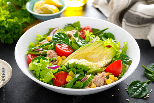 Avocado and tuna fresh vegetable salad with tomato, cucumber corn, onion, lettuce and spinach. Healthy and detox food concept. Ketogenic diet. Buddha bowl dish on black background.