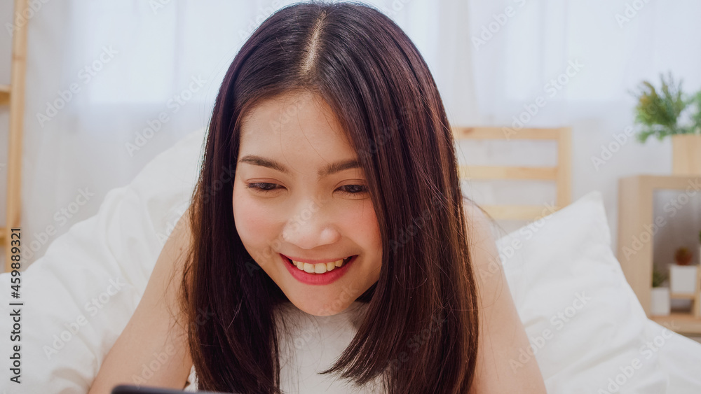 Young Asian woman using smartphone checking social media feeling happy smiling while lying on bed after wake up in the morning, Beautiful attractive Japanese girl smiling relax in bedroom at home. Young Asian woman using smartphone checking social media feeling happy smiling while lying on bed after wake up in the morning, Beautiful attractive Japanese girl smiling relax in bedroom at home.