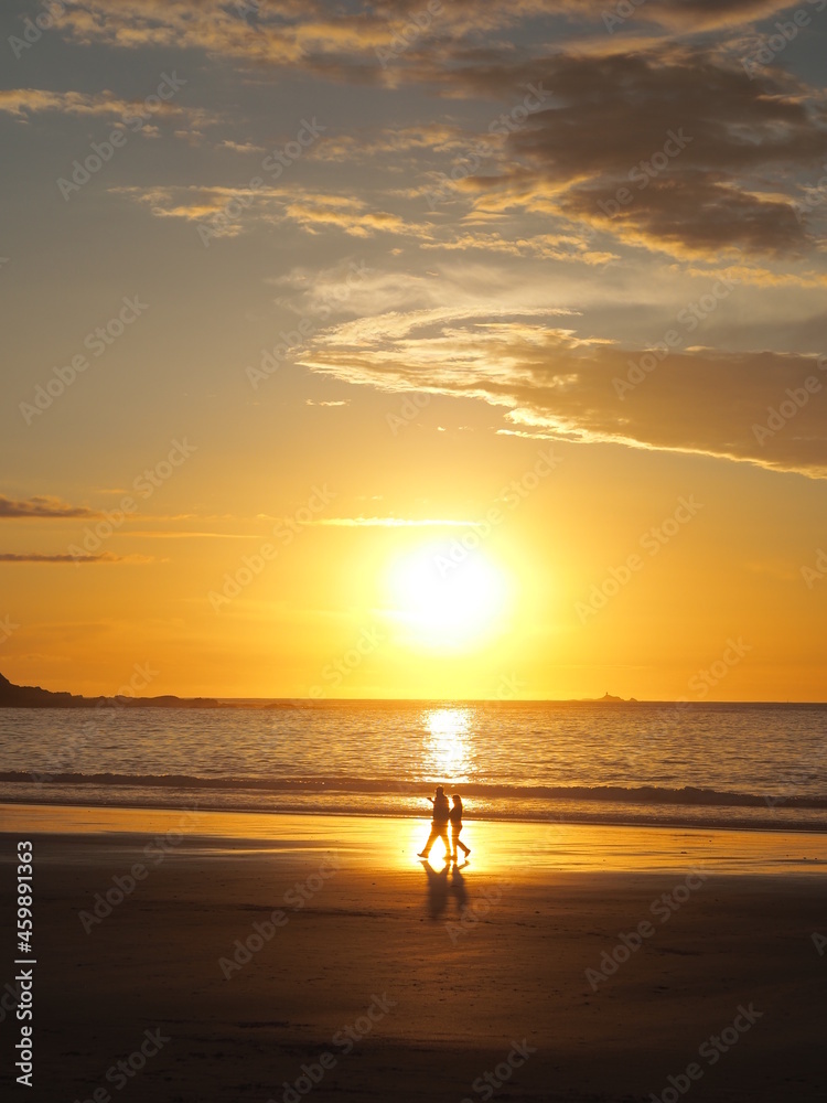 A couple walks alone in the beach with the sunset in the background