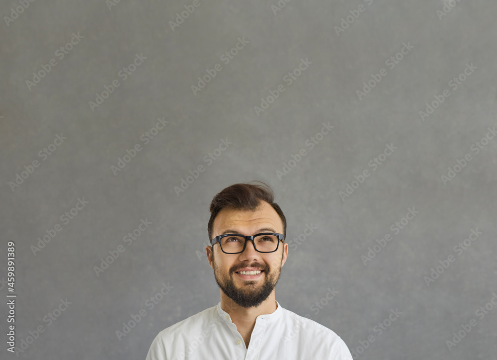 Close up portrait of thoughtful young pensive businessman looking up on grey studio copy space. Caucasian smiling male person has dreamy expression, planning future, thinking about great idea in mind Close up portrait of thoughtful young pensive businessman looking up on grey studio copy space. Caucasian smiling male person has dreamy expression, planning future, thinking about great idea in mind