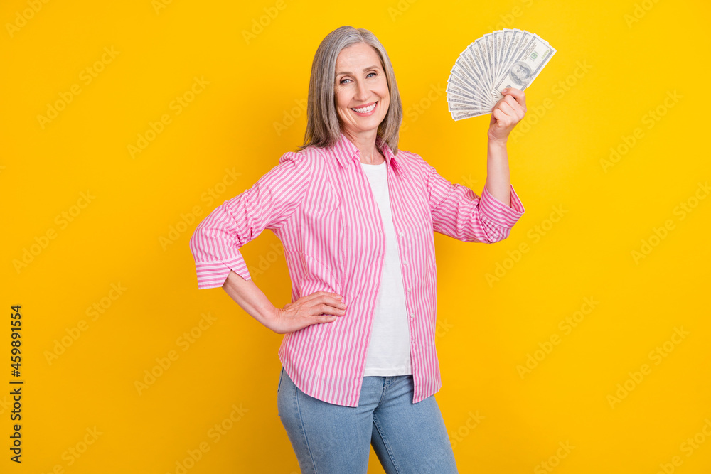Profile side photo of aged woman happy positive smile wealthy hold money cash isolated over yellow color background Profile side photo of aged woman happy positive smile wealthy hold money cash isolated over yellow color background