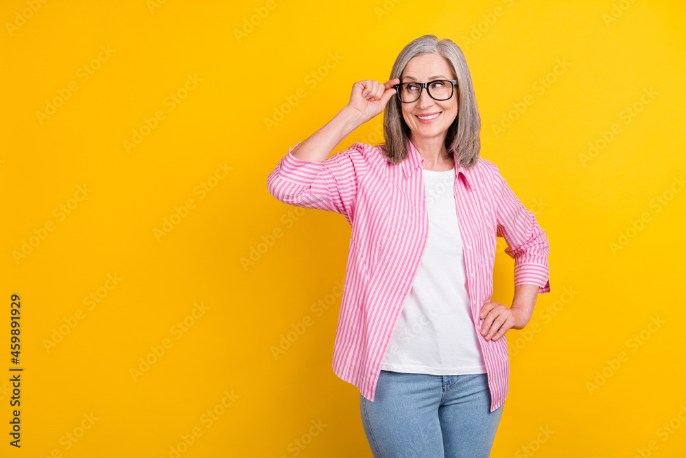 Photo of aged woman happy positive smile hand touch eyeglasses look empty space isolated over yellow color background Photo of aged woman happy positive smile hand touch eyeglasses look empty space isolated over yellow color background