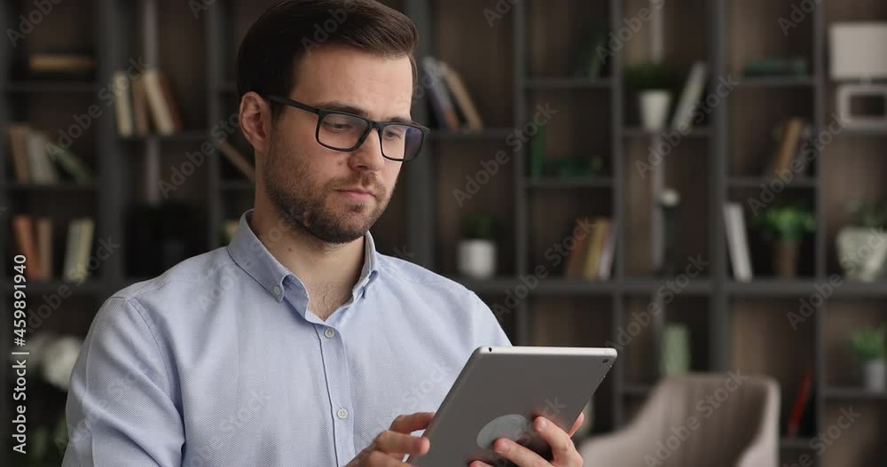 Concentrated millennial businessman in eyewear using digital computer software applications, typing email for colleagues or working on online project in modern office room, modern gadgets usage. Concentrated millennial businessman in eyewear using digital computer software applications, typing email for colleagues or working on online project in modern office room, modern gadgets usage.