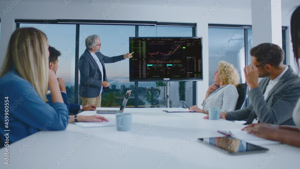 Management meeting. Mature adult man giving presentation to colleagues. Showing and explaining financial chart. Modern open space office interior.