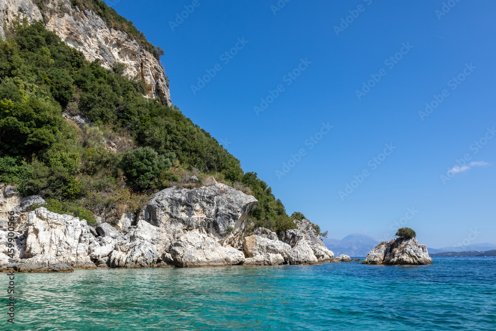 Turquoise Ionian Sea with scenic green cliffs, rocks in water and bright sky. Nature of Ormos Desimi, Lefkada island in Greece. Summer vacation idyllic travel destination