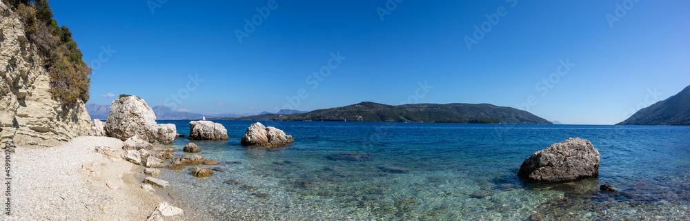 Wide panorama of white pebbles and rocks beach with azure clear water on coast of Lefkada island in Greece. Summer wild nature vacation travel to Ionian Sea