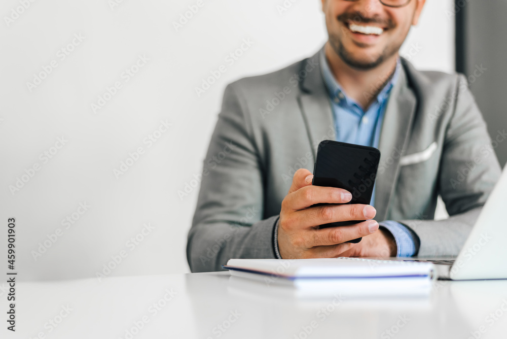 Top cut portrait of a cheerful man using smart phone at home, or cellphone at office desk. Small business entrepreneur looking at his mobile phone and smiling. Top cut portrait of a cheerful man using smart phone at home, or cellphone at office desk. Small business entrepreneur looking at his mobile phone and smiling.