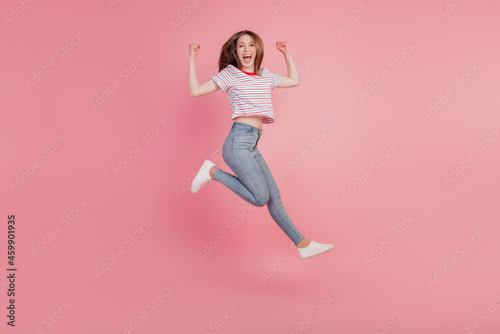 Portrait of astonished pretty winner lady jump raise fists run on pink background