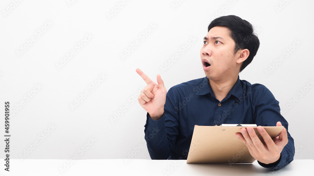 Asian man holding document board at the table feeling shocked point finger at copy space Asian man holding document board at the table feeling shocked point finger at copy space