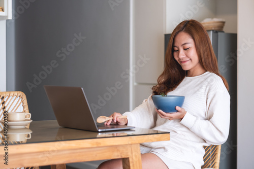 A woman eating food while using laptop computer for working or studying online at home