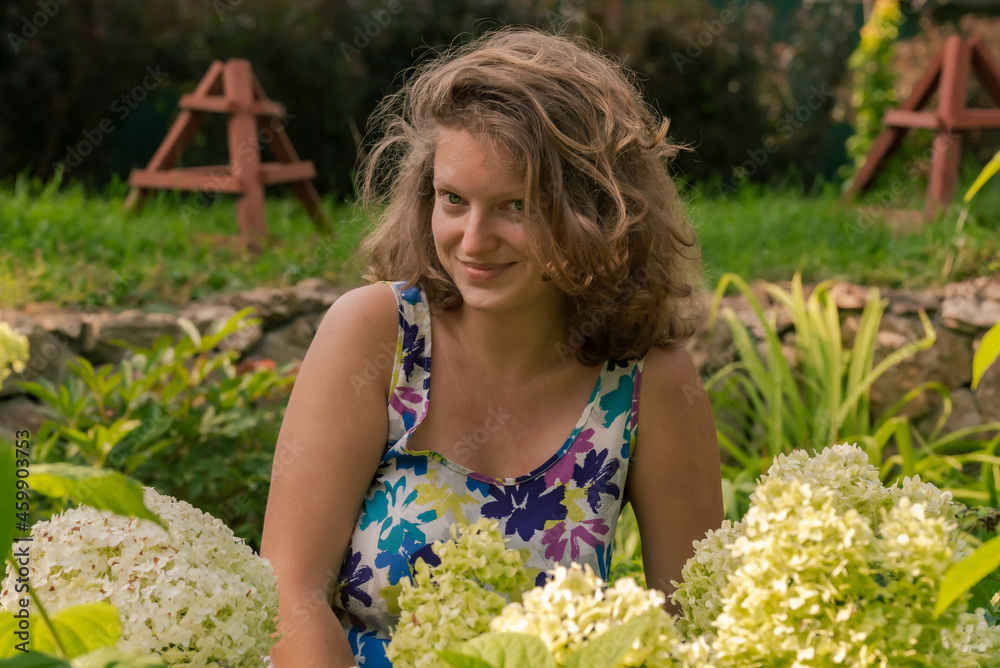 Young woman in the garden among white hydrangea flowers