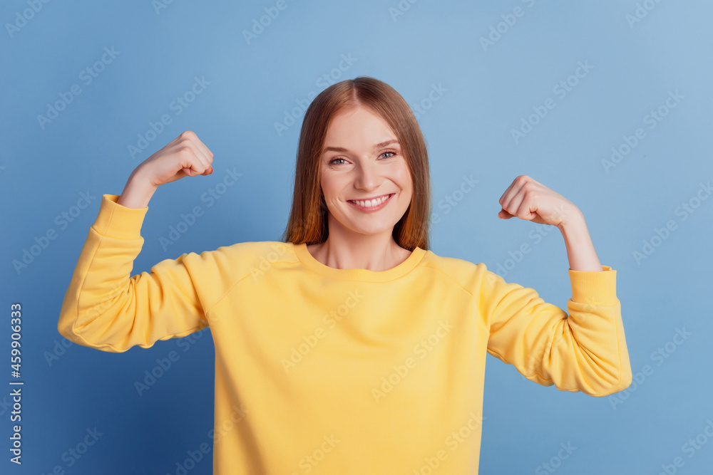 Fototapeta premium Portrait of fit slim sportive active lady show hand muscles toothy smile on blue background