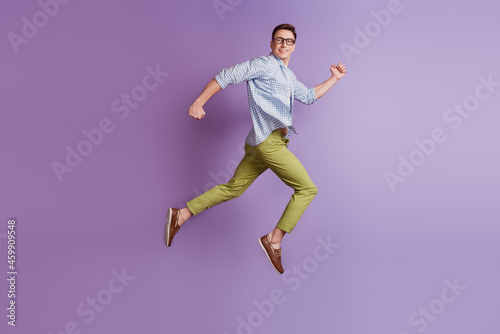 Portrait of jumper energetic active guy jump run look back empty space on violet background © Tetiana