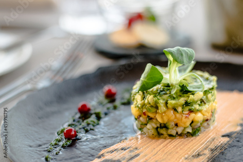 Cuadro en lienzo Colorful avocado tartar on a black plate at a restaurant