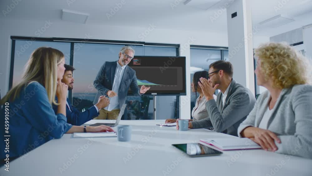Low angle view of people discussing at meeting. Colourful chars on large screen in background. Modern open space office interior.