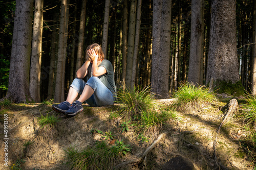 Frau sitzt auf dem Boden im Wald und hält sich verzweifelt die Hände vor ihr Gesicht. Depression, Herbst. 