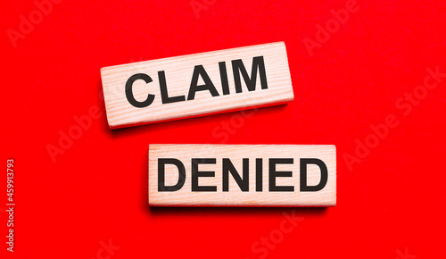 On a bright red background, there are two light wooden blocks with the text CLAIM DENIED