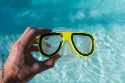 Yellow swimming goggles next to a clear blue rippled swimming pool