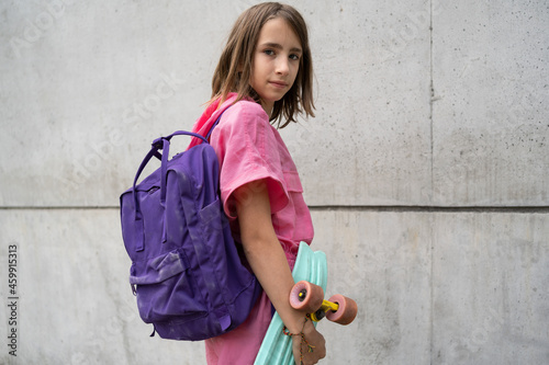 Tennage girl with a skateboard and schoolbag looking at camera