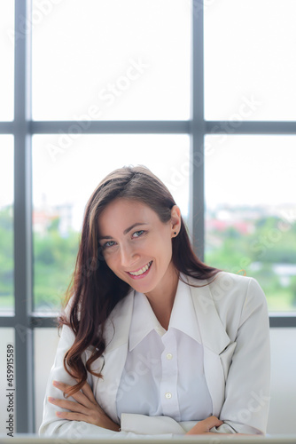 Free Download Close-up Portrait of a confidence and smiling Caucasian businesswoman in white suit look Cheerful and friendly demeanor. sitting in a modern office.Start-up modern office or workplace background. - GFXLoad