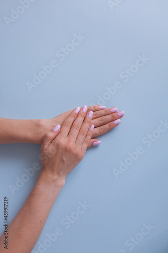 Elegant hands with pink manicure on a blue background, clean color, white skin.