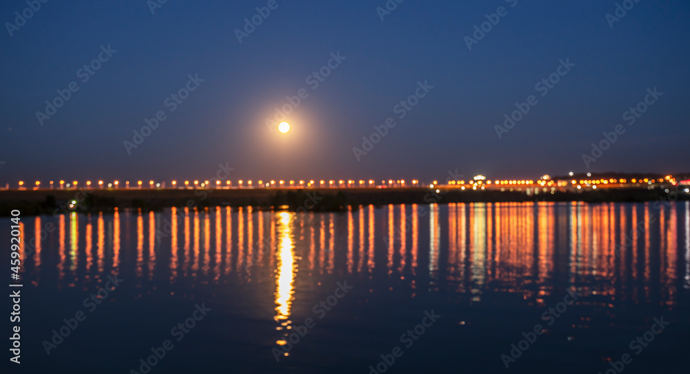 pier at sunset, Illumination at the dam of the hydroelectric power station as a background and moon road. Selective focus.
