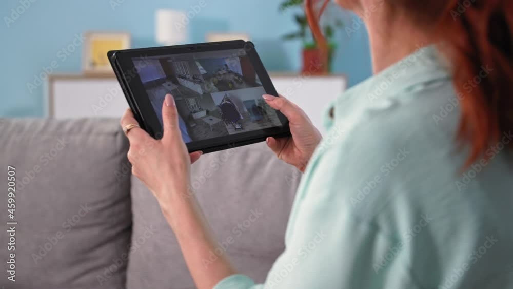 close up of back view of young woman using home security camera system in apartment, girl with tablet pc and cam in hands sits on couch