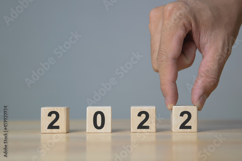 Hand of man putting wood cube 2022. New year concept.
