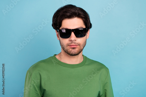 Portrait of handsome serious peaceful man wear sunglass green pullover isolated on blue color background