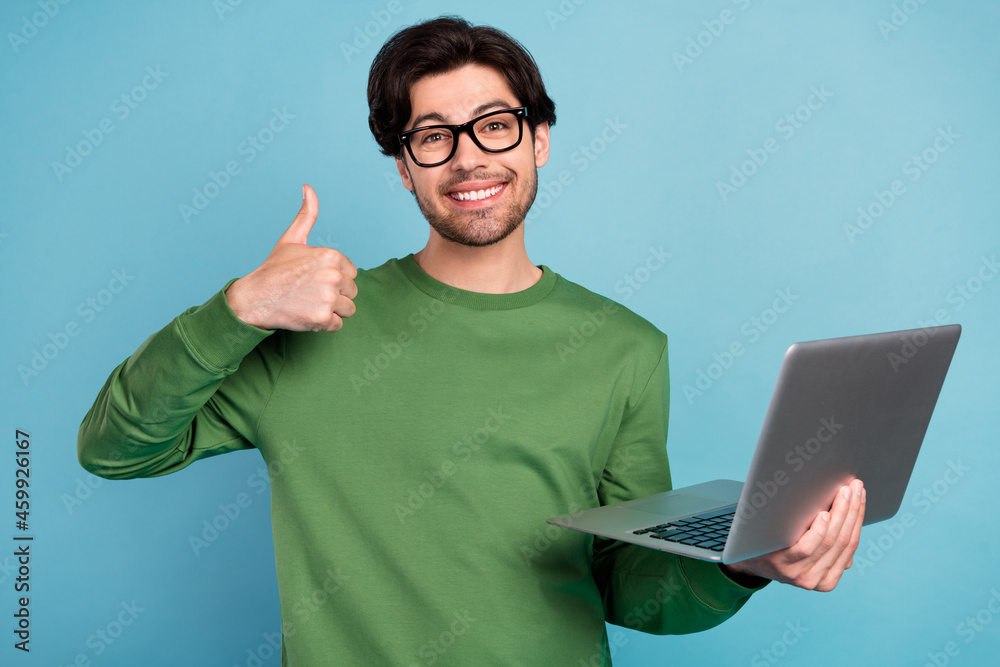 Portrait of smiling geek nerd young businessman in glasses show thumb-up hold laptop isolated on blue color background Portrait of smiling geek nerd young businessman in glasses show thumb-up hold laptop isolated on blue color background