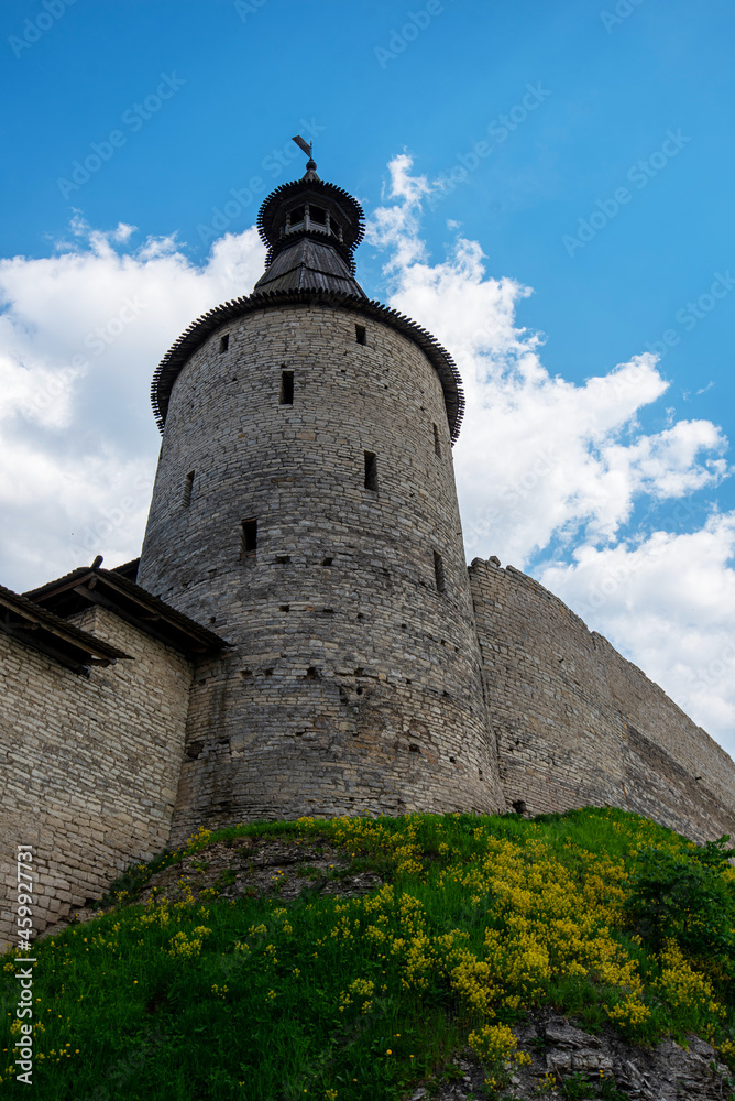 The fortress wall of a medieval fortification with towers against a bright blue sky.