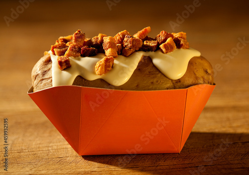 Batata assada e recheada com requeijão e cubos de bacon no fundo de madeira rústica.
