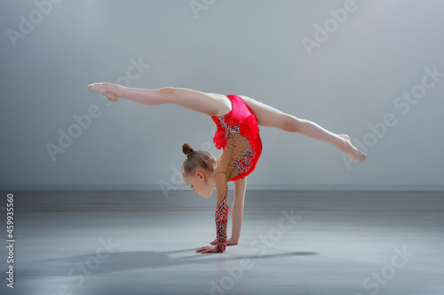 Image of flexible little girl doing exercise on hands in pink sportwear in gray studio