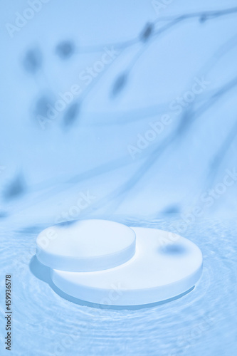 Pastel blue colored abstract nature scene with white cylinder podium on transparent water with waves and soft shadow of plants. Pedestal for cosmetic product and packaging mockups display presentation