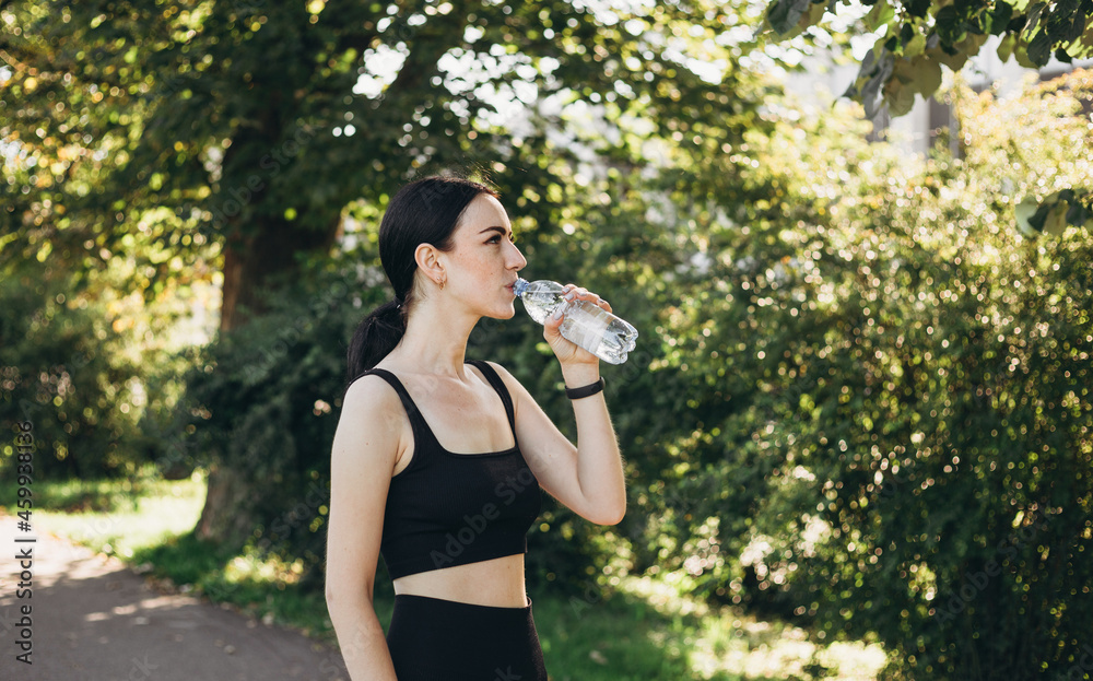 Athletic young woman after runing in the park jogging in the morning for lifestyle health. Female runner standing outdoors holding water bottle. Fitness woman taking a break after running workout. Athletic young woman after runing in the park jogging in the morning for lifestyle health. Female runner standing outdoors holding water bottle. Fitness woman taking a break after running workout.
