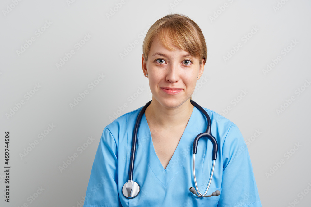 Young female medic nursing assistant with phonendoscope in blue uniform looking at camera. Smiling expert emergency in hospital. Clinic resident physician. Trustworthy paramedic. Internship practice Young female medic nursing assistant with phonendoscope in blue uniform looking at camera. Smiling expert emergency in hospital. Clinic resident physician. Trustworthy paramedic. Internship practice