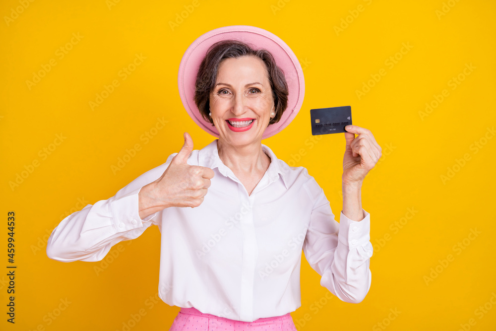 Photo of mature business woman happy positive smile thumb-up like advert choice credit card isolated over yellow color background Photo of mature business woman happy positive smile thumb-up like advert choice credit card isolated over yellow color background