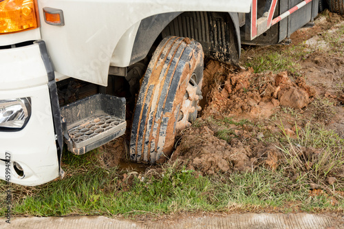 Wheel of a heavy truck lorry stuck in deep mud soft ground. Muddy and soft soil road at construction site after raining.