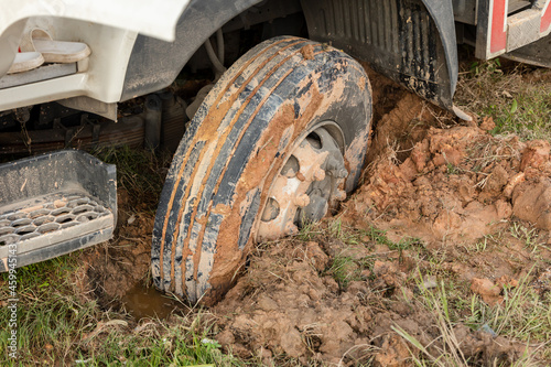 Wheel of a heavy truck lorry stuck in deep mud soft ground. Muddy and soft soil road at construction site after raining.