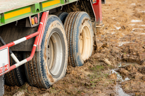 Wheel of a heavy truck lorry stuck in deep mud soft ground. Muddy and soft soil road at construction site after raining.