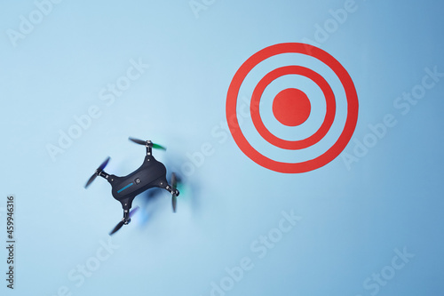 Aerial top down view on isolated drone copter with spinning propellers flying in the direction of the red target on the bright solid blue fond background