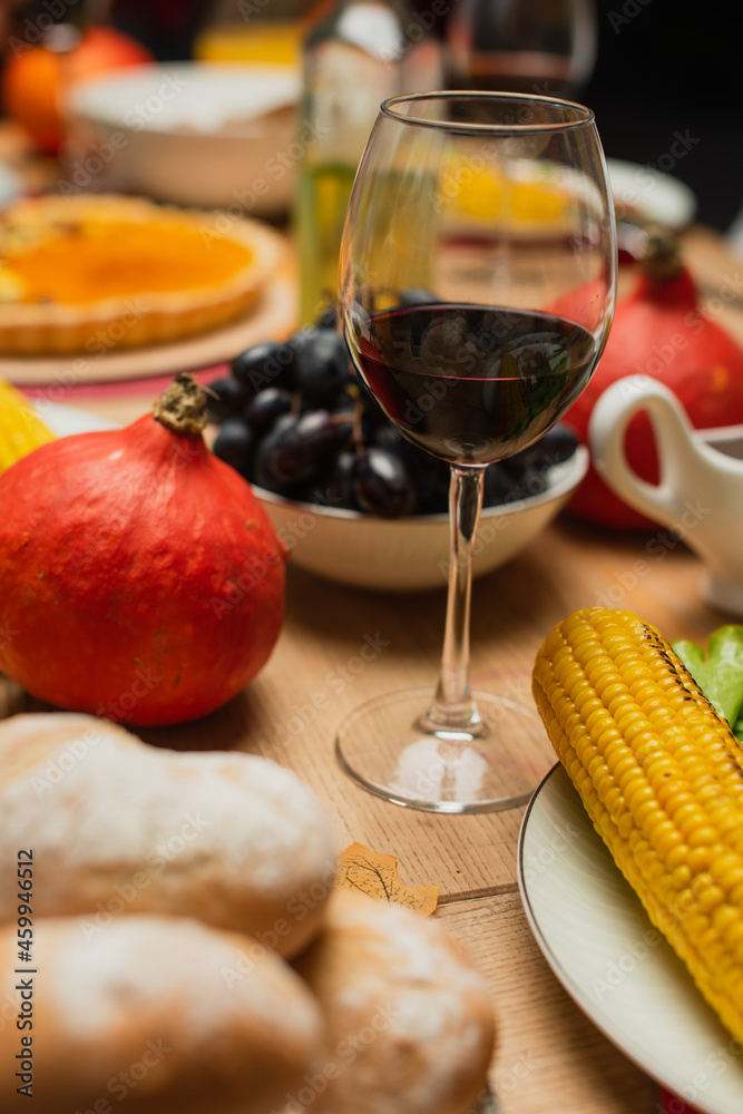 glass of red wine near whole pumpkin, grilled corn and fresh grape on table served with thanksgiving day