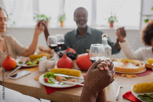 selective focus of african american woman and boy holding hands while praying with blurred family near served table
