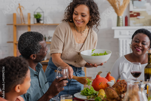 African american woman pouring salad near family and son during thanksgiving celebration
