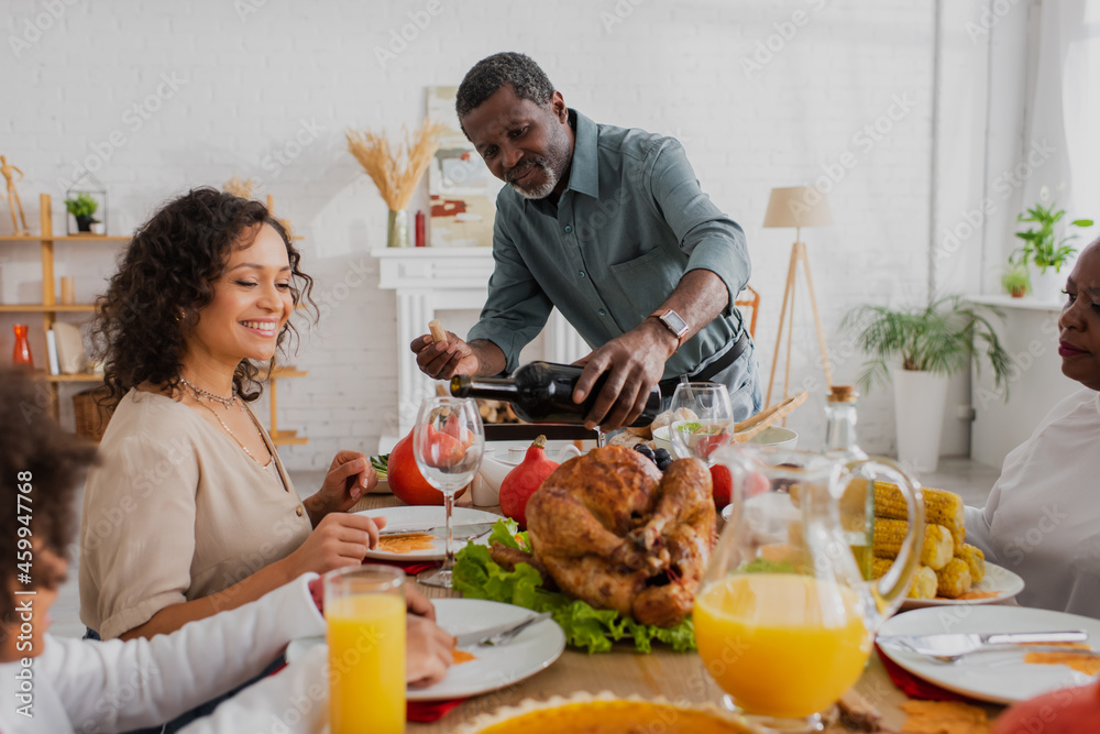 African american man pouring wine near family and thanksgiving dinner