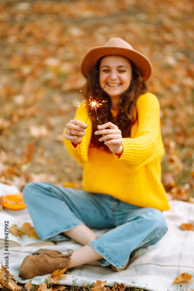 Fototapeta premium Glowing sparkles in hands. Young woman in a yellow sweater with Christmas sparklers on nature. Autumn style. 