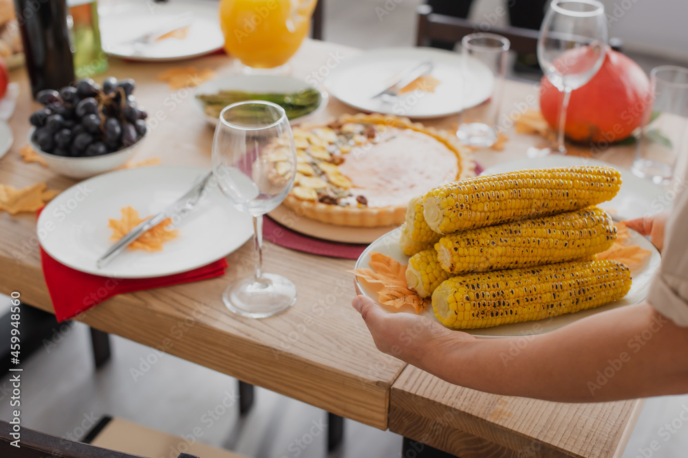 Cropped view of african american woman holding baked corn near thanksgiving dinner Cropped view of african american woman holding baked corn near thanksgiving dinner